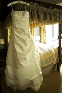 wedding dress hanging from four poster bed with morning sunlight streaming through windows